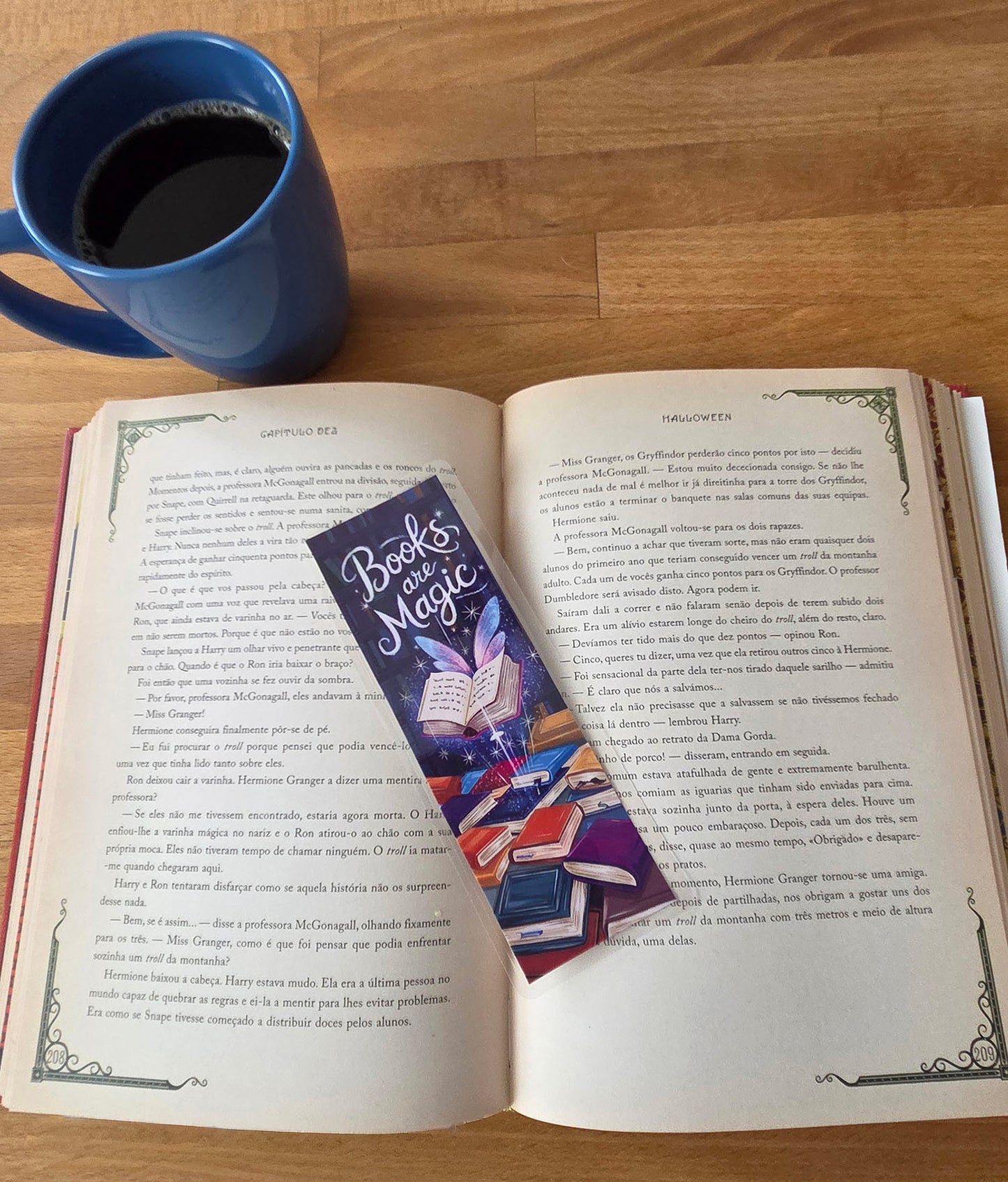 Open book with a bookmark titled 'Books are Magic' on a wooden surface next to a blue mug.